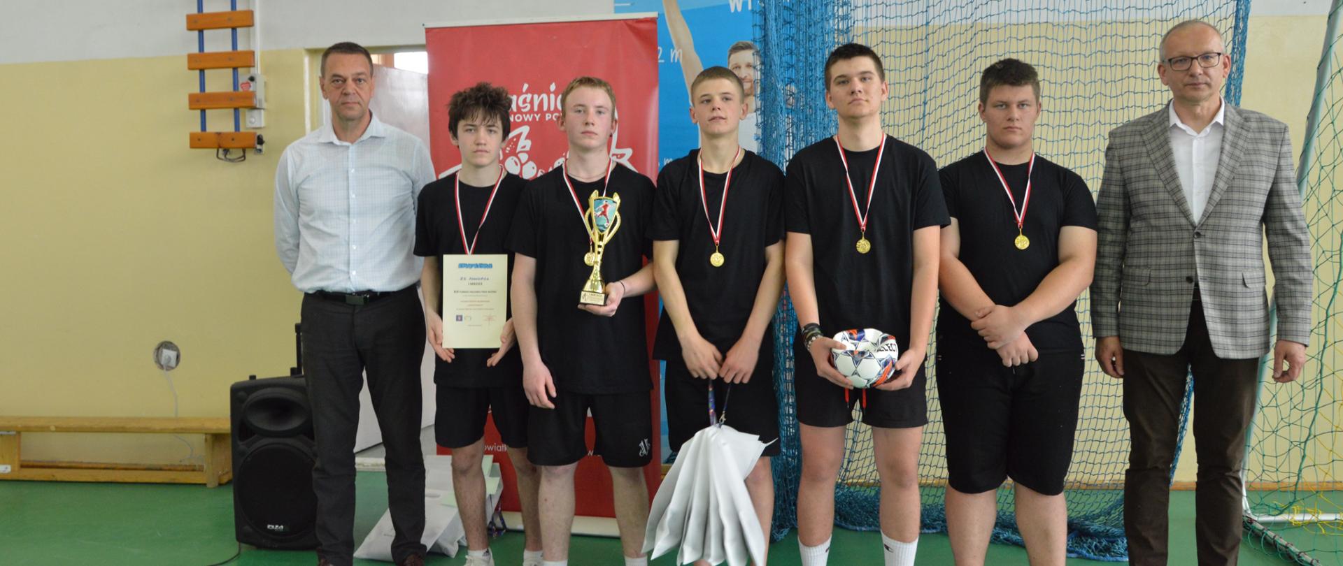 Pięciu zawodników Zespołu Szkół w Annopolu z zawieszonymi medalami na szyjach oraz nagrodami: piłką nożną, pucharem, dyplomem i torbami prezentowymi. Pierwszy z prawej strony stoi Członek Zarządu Powiatu w Kraśniku Marek Kołtun. Pierwszy z lewej stoi Dyrektor Zespołu Szkół w Annopolu Zbigniew Siewierski