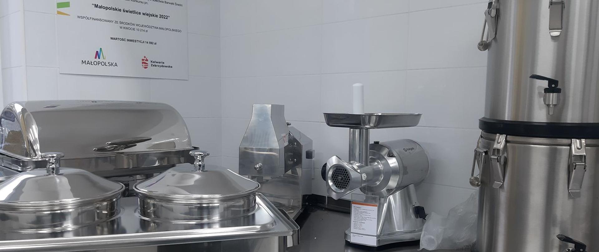 Wyposażenie kuchni widoczne 2 kociołki podgrzewane paliwem, podgrzewacz do potraw, maszynkę do mielenia mięsa, warnik do wody, kotleciarkę elektryczną, 2 termosy z kranem 