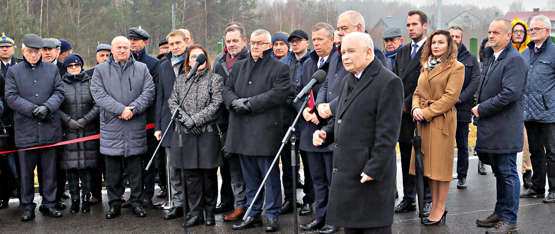 Wiceprezes Rady Ministrów Jarosław Kaczyński przemawia. Z nim stoją zaproszeni goście na uroczyste otwarcie obwodnicy Janowa Lubelskiego. W oficjalnym otwarciu trasy wzięli udział między innymi Wiceprezes Rady Ministrów, Minister Aktywów Państwowych Jacek Sasin, Minister Infrastruktury Andrzej Adamczyk, Zastępca Szefa Kancelarii Prezydenta Rzeczpospolitej Polskiej Piotr Ćwik, Poseł do Europarlamentu Elżbieta Mazurek, Wojewoda Lubelski Lech Sprawka, Marszałek Województwa Lubelskiego Jarosław Stawiarski, Poseł na Sejm RP Kazimierz Choma, Radna Sejmiku Województwa Lubelskiego Anna Baluch, Starosta Kraśnicki Andrzej Rolla.