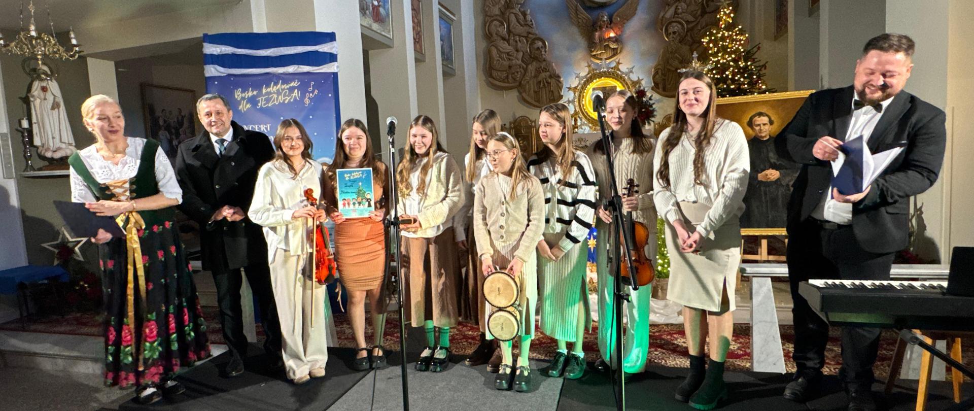 Moment odebrania dyplomów. Dwoje prowadzących oraz po środku grupa dziewczyn z Panem Wójtem Tomaszem Rajcą . 