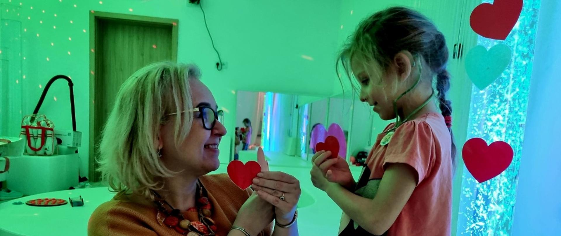 Zajęcia w sali - Pani Dyrektor wraz z dziewczynką uśmiechają się do siebie, trzymają w rękach papierowe serca