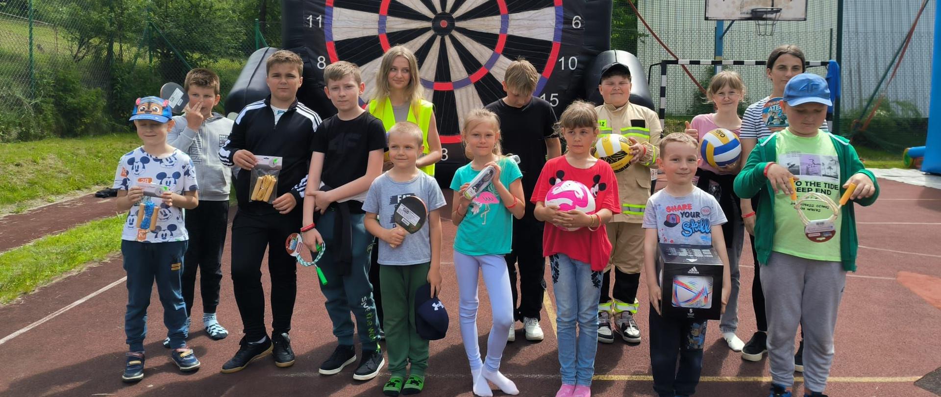 Zdjęcie przedstawia grupkę dzieci pozujący z nagrodami na boisku podczas imprezy z okazji Dnia Dziecka