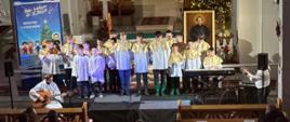 Grupa ministrantów śpiewa kolędę, jeden gra na gitarze. 