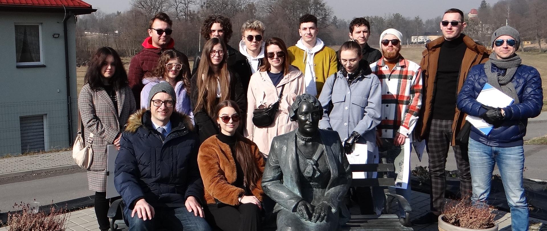 Goście z Katowic z wójtem Grzegorzem Sikorskim przy pomniku-ławeczce hrabiny Gabrieli Thun-Hohenstein. Grupa osób pozuje do zdjęcia. Dwie osoby siedzą, reszta stoi