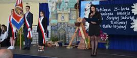 Przemowa Pani Dyrektor na scenie na akademii. W tle scenografia zamek oraz tytuł Jubileuszu.