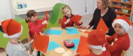 Warsztaty plastyczne - dzieci siedzą przy stole z panią nauczycielką i wspólnie wycinają świąteczne ozdoby